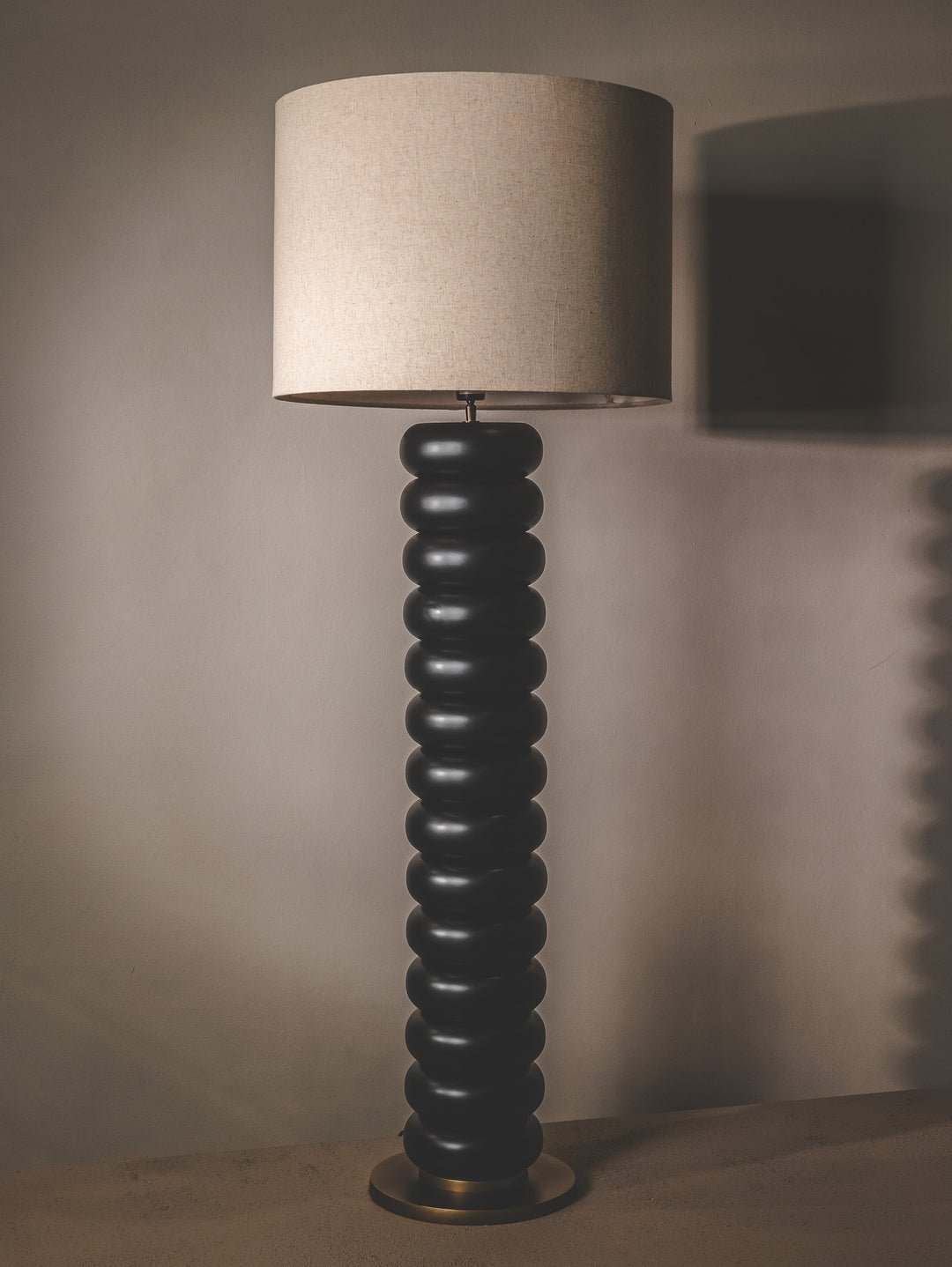 Black floor lamp with bobbin-style base and linen shade.