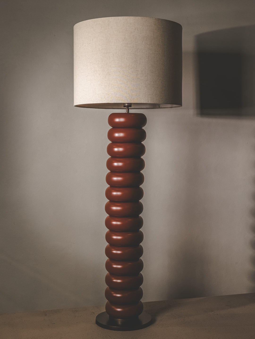 Rust floor lamp with bobbin-style base and linen shade.